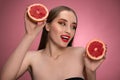 Beautiful young woman model holding two juicy grapefruit sliced in half in her hands looking sideways. Charming joyful