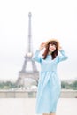 Beautiful young woman model wearing stylish hat and blue dress, posing in front of the Eiffel tower in Paris, France Royalty Free Stock Photo