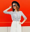 Beautiful young woman model wearing white striped shirt, black round hat posing on city street over red wall Royalty Free Stock Photo