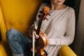 Beautiful young woman musician posing with a violin in a soft chair Royalty Free Stock Photo