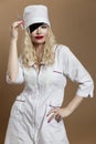 Beautiful young woman in nurse uniform with a syringe in her hand and a black eye patch. Sexy blonde with red lips. Compulsory Royalty Free Stock Photo