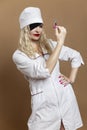 Beautiful young woman in nurse uniform with a syringe in her hand and a black eye patch. Sexy blonde with red lips. Compulsory Royalty Free Stock Photo