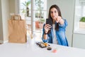 Beautiful young woman ordering food delivery from app using smartphone pointing with finger to the camera and to you, hand sign, Royalty Free Stock Photo
