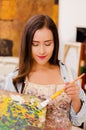 Beautiful young woman painter with color palette and paint brush in hand, in a blurred background