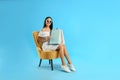 Beautiful young woman with paper shopping bags in armchair on light blue background Royalty Free Stock Photo