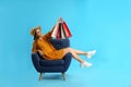 Beautiful young woman with paper shopping bags in armchair on light blue background Royalty Free Stock Photo