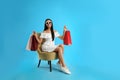 Beautiful young woman with paper shopping bags in armchair on light blue background Royalty Free Stock Photo