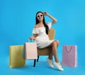 Beautiful young woman with paper shopping bags in armchair on light blue background Royalty Free Stock Photo