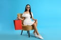 Beautiful young woman with shopping bags in armchair on light blue background Royalty Free Stock Photo