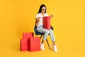 Beautiful young woman with paper shopping bags in armchair on yellow background Royalty Free Stock Photo