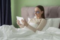 Beautiful young woman with patches on her eyes is lying on the bed in the bedroom at home and using a tablet. Royalty Free Stock Photo