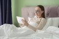 Beautiful young woman with patches on her eyes is lying on the bed in the bedroom at home and using a tablet. Royalty Free Stock Photo