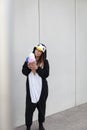 Beautiful, young woman in penguin costume is eating decoration ice cream in front of concrete wall Royalty Free Stock Photo