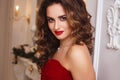 Beautiful young woman with perfect make up and hair style in gorgeous red evening dress in expensive luxury interior