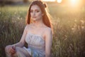 Beautiful young woman with perfect make up and long plaited hair sitting in the field at sunset