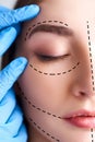 Beautiful young woman with perforation lines on her face before plastic surgery operation. Beautician hands in gloves Royalty Free Stock Photo