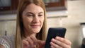 Beautiful young woman with a phablet sitting in kitchen. Browsing Internet and smiling.