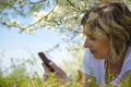 Beautiful young woman with a phone, lying on the field, green grass and flowers. Outdoors enjoy nature. Healthy smiling girl lying Royalty Free Stock Photo