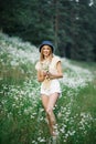 Beautiful young woman picking white wildflowers on the background of a forest landscape in summer. Portrait of a gentle happy