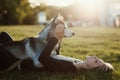 Beautiful young woman playing with funny husky dog outdoors in park at sunset or sunrise