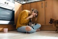 Beautiful young woman playing with her cute lovely animals sitting on the floor in the kitchen at home