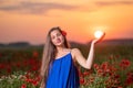 Beautiful young woman playing with sun ball while standing in poppy field in warm sunset light Royalty Free Stock Photo