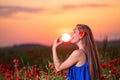 Beautiful young woman playing with sun ball while standing in poppy field in warm sunset light Royalty Free Stock Photo