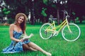 Beautiful young woman portrait reading a book with bicycle in the park.