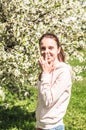 Beautiful young woman posing near spring flowering trees. Girl touches her nose by the finger. Allergy free concept. Model in Royalty Free Stock Photo