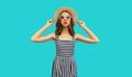 Beautiful young woman posing wearing summer straw hat, striped dress on blue background Royalty Free Stock Photo