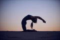 Beautiful young woman practices advanced variation of camel pose - Ustrasana in the desert at night