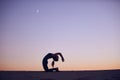 Beautiful young woman practices advanced variation of camel pose - Ustrasana in the desert at night