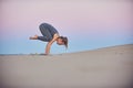 Beautiful young woman practices yoga asana Bakasana - crane pose in the desert at sunset