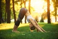 Beautiful young woman practices yoga asana downward facing dog in the park at sunset