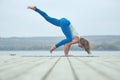 Beautiful young woman practices yoga asana Eka Pada Bakasana - one leg crane pose on the wooden deck near the lake