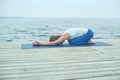 Beautiful young woman practices yoga asana Balasana - child`s pose on the wooden deck near the lake Royalty Free Stock Photo