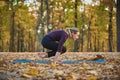 Beautiful young woman practices yoga asana Lolasana Pendant pose on the wooden deck in the autumn park.