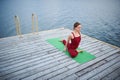 Beautiful young woman practices yoga asana One Legged King Pigeon Pose - Eka Pada Rajakapotasana on the wooden deck near the lake Royalty Free Stock Photo