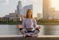 Beautiful young woman practices yoga asana Padangustha Padma Utkatasana - Half Lotus Toe Balance pose outdoors against