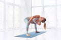 Beautiful young woman practices yoga asana Parivritta Stupasana at the yoga class