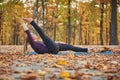 Beautiful young woman practices yoga asana Supta Padangushthasana 1 on the wooden deck in the autumn park.