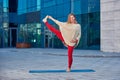 Beautiful young woman practices yoga asana Utthita Hasta Padangushthasana outdoors against the background of a modern city