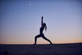 Beautiful young woman practices yoga asana Virabhadrasana 1 - warrior pose 1 in the desert at night Royalty Free Stock Photo