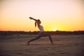 Beautiful young woman practices yoga asana Virabhadrasana 1 - warrior pose 1 in the desert at sunset Royalty Free Stock Photo