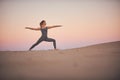 Beautiful young woman practices yoga asana Virabhadrasana 2 - warrior pose 2 in the desert at sunset Royalty Free Stock Photo