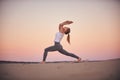 Beautiful young woman practices yoga asana Virabhadrasana 1 - warrior pose 1 in the desert at sunset Royalty Free Stock Photo