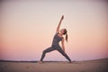 Beautiful young woman practices yoga asana Virabhadrasana 2 - warrior pose 2 in the desert at sunset Royalty Free Stock Photo