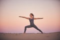 Beautiful young woman practices yoga asana Virabhadrasana 2 - warrior pose 2 in the desert at sunset Royalty Free Stock Photo