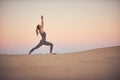 Beautiful young woman practices yoga asana Virabhadrasana 1 - warrior pose 1 in the desert at sunset Royalty Free Stock Photo