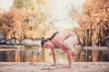 Beautiful young woman practices yoga asana on the wooden desk in the autumn park.
